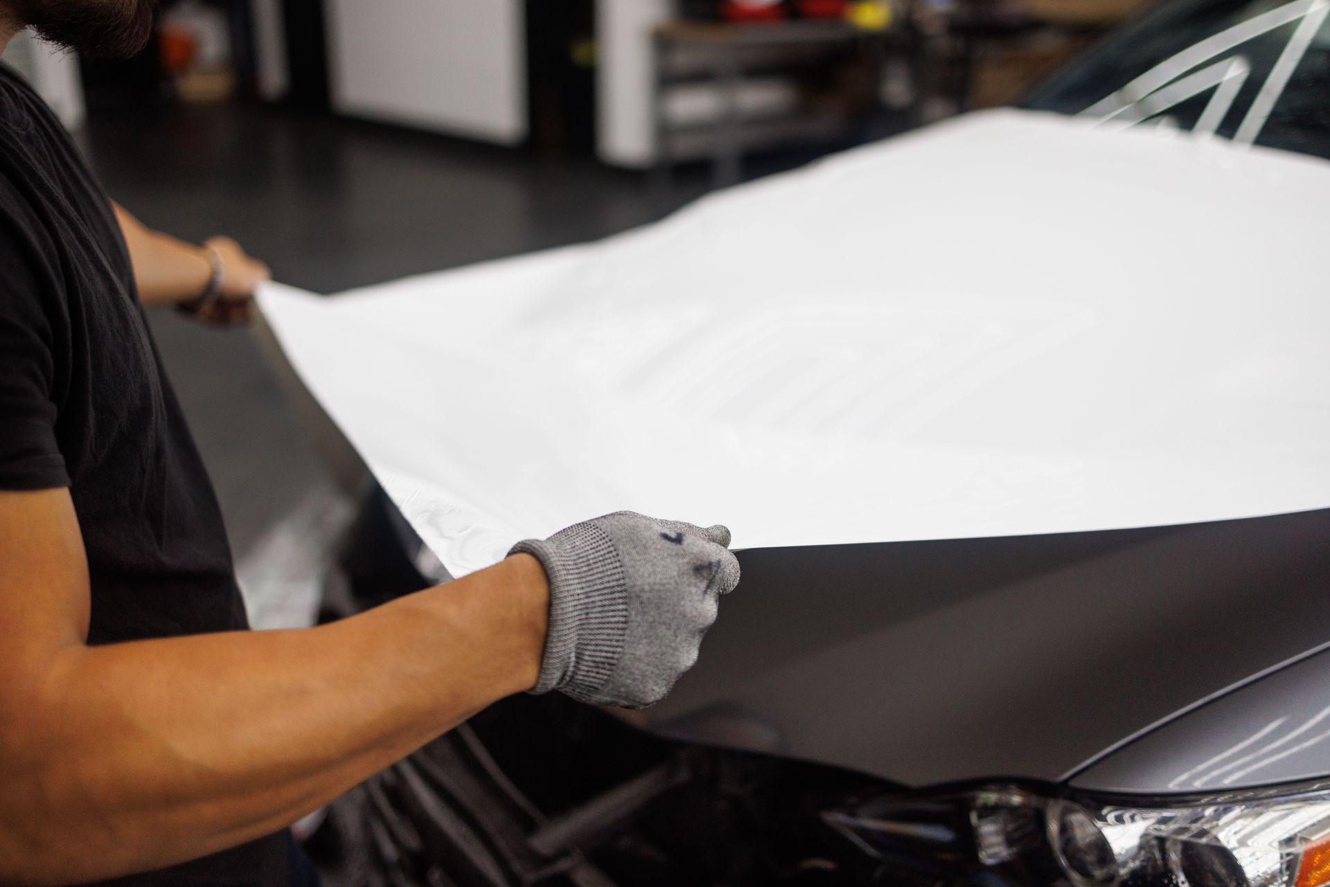 Gloved hands applying a white sheet to a car hood in a workshop