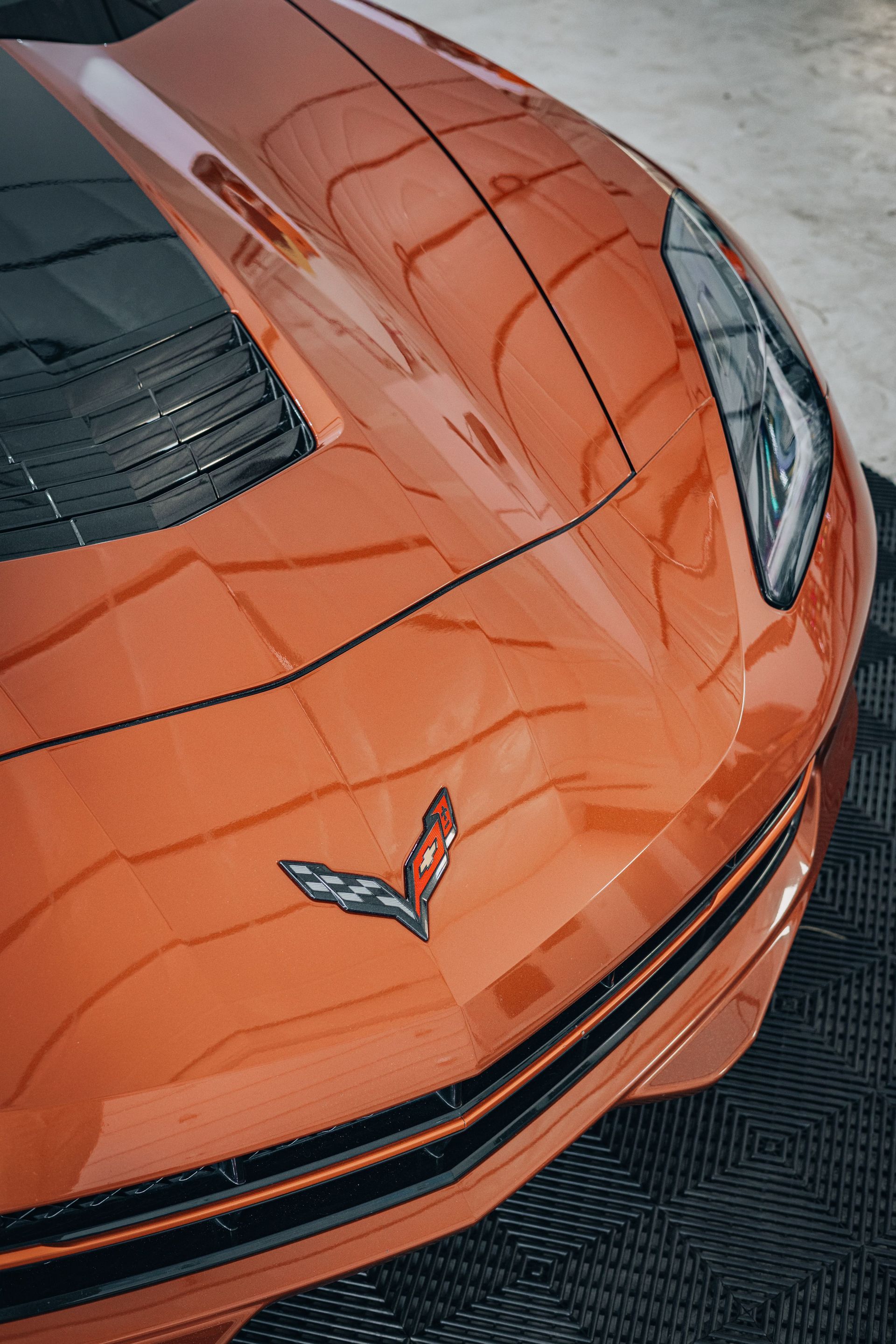 Orange Chevrolet Corvette front hood and emblem, parked on a textured surface.