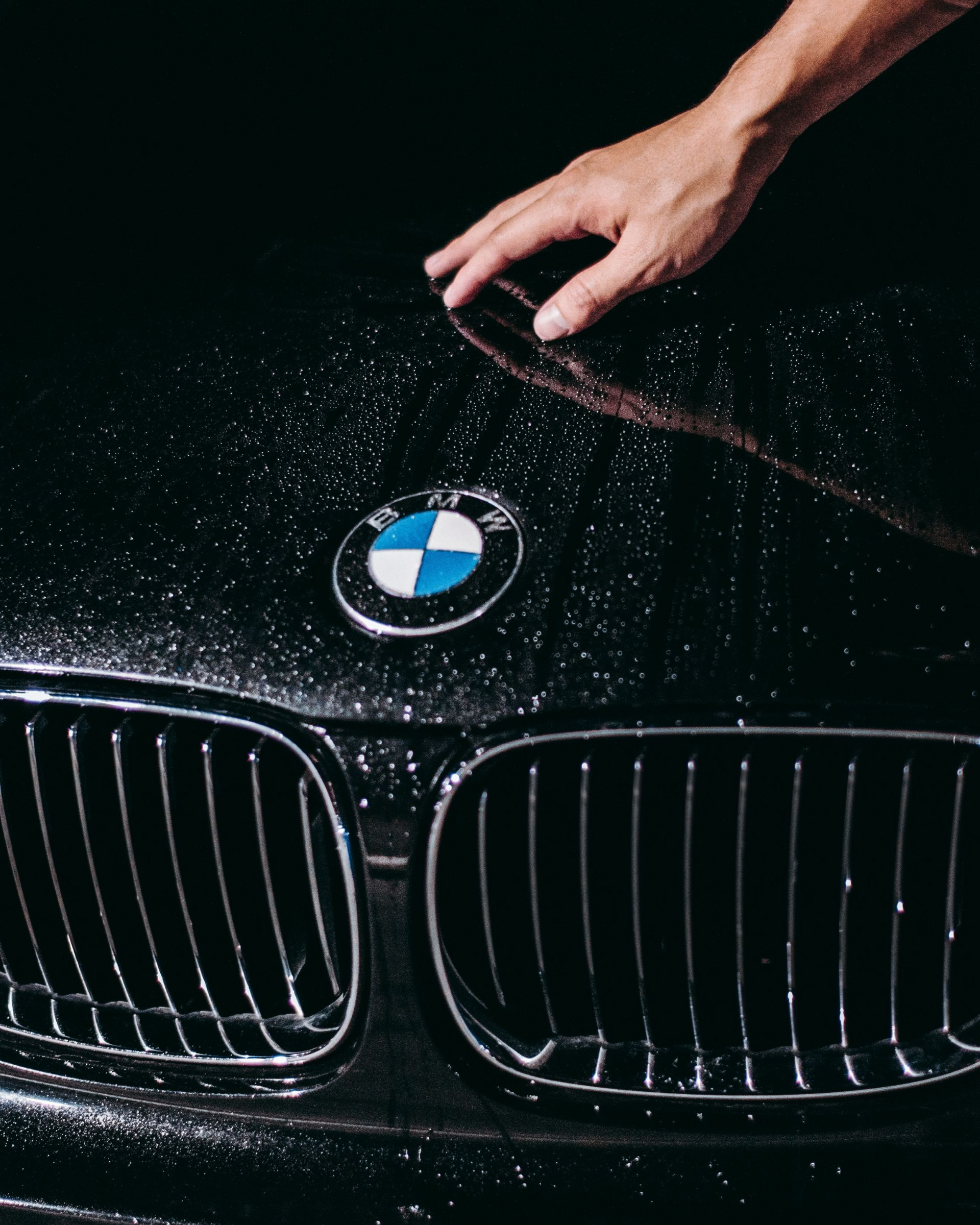 Hand wiping a wet black BMW hood with the emblem visible