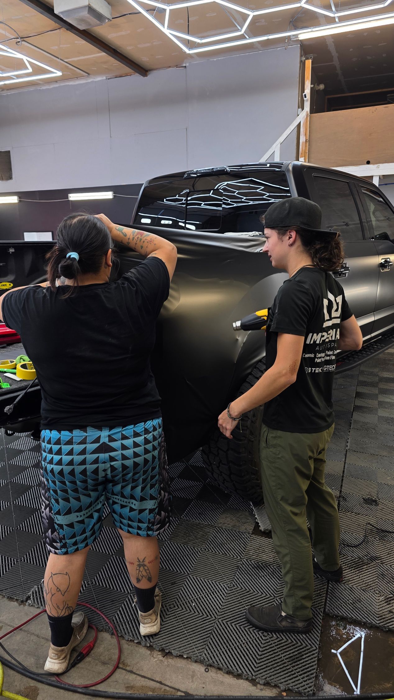 Dark teal pickup truck with a lifted front wheel displayed indoors under geometric ceiling lights.
