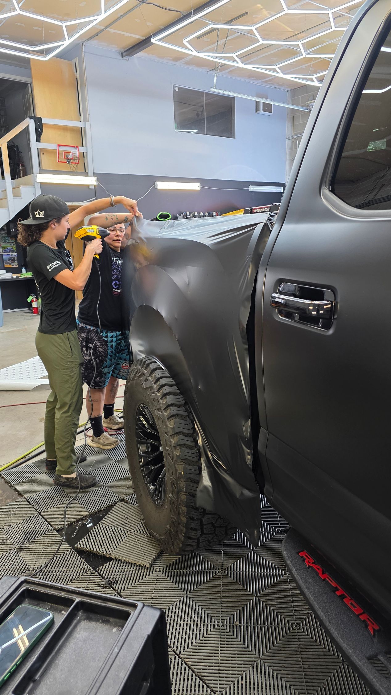 Two children pose beside a black lifted truck in a garage workshop