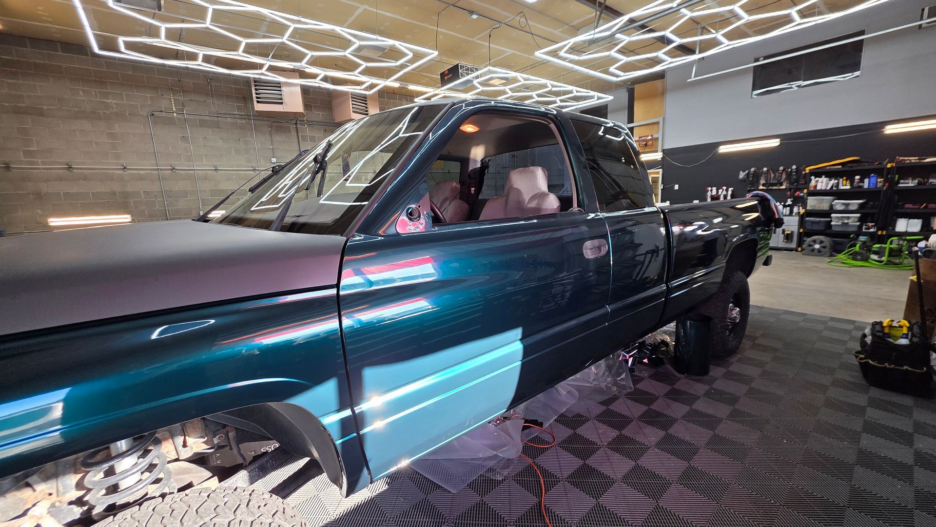 Shiny teal pickup truck on display in a modern showroom with geometric ceiling lights