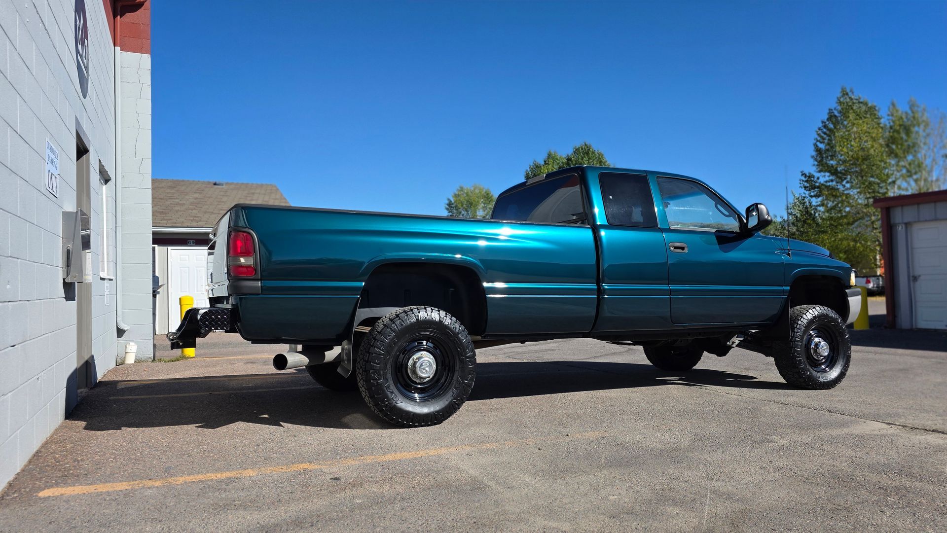 Teal pickup truck parked beside a building on a sunny day