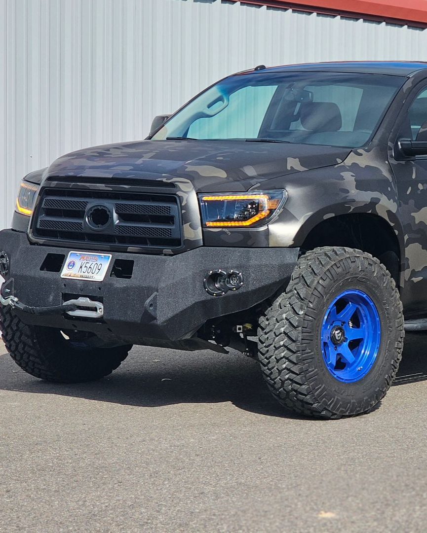 Black lifted pickup truck with blue wheels parked beside a metal building.