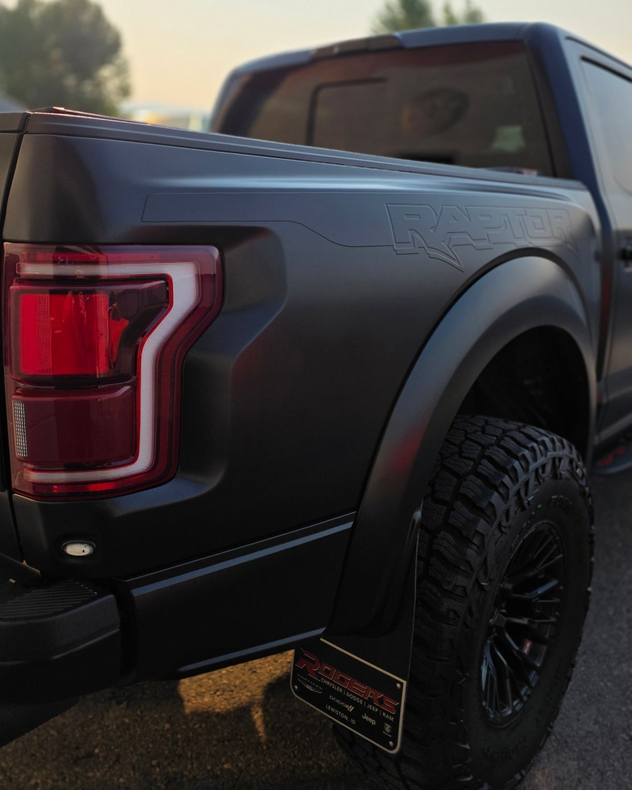 Matte black pickup truck close-up with off-road tires and red taillight.