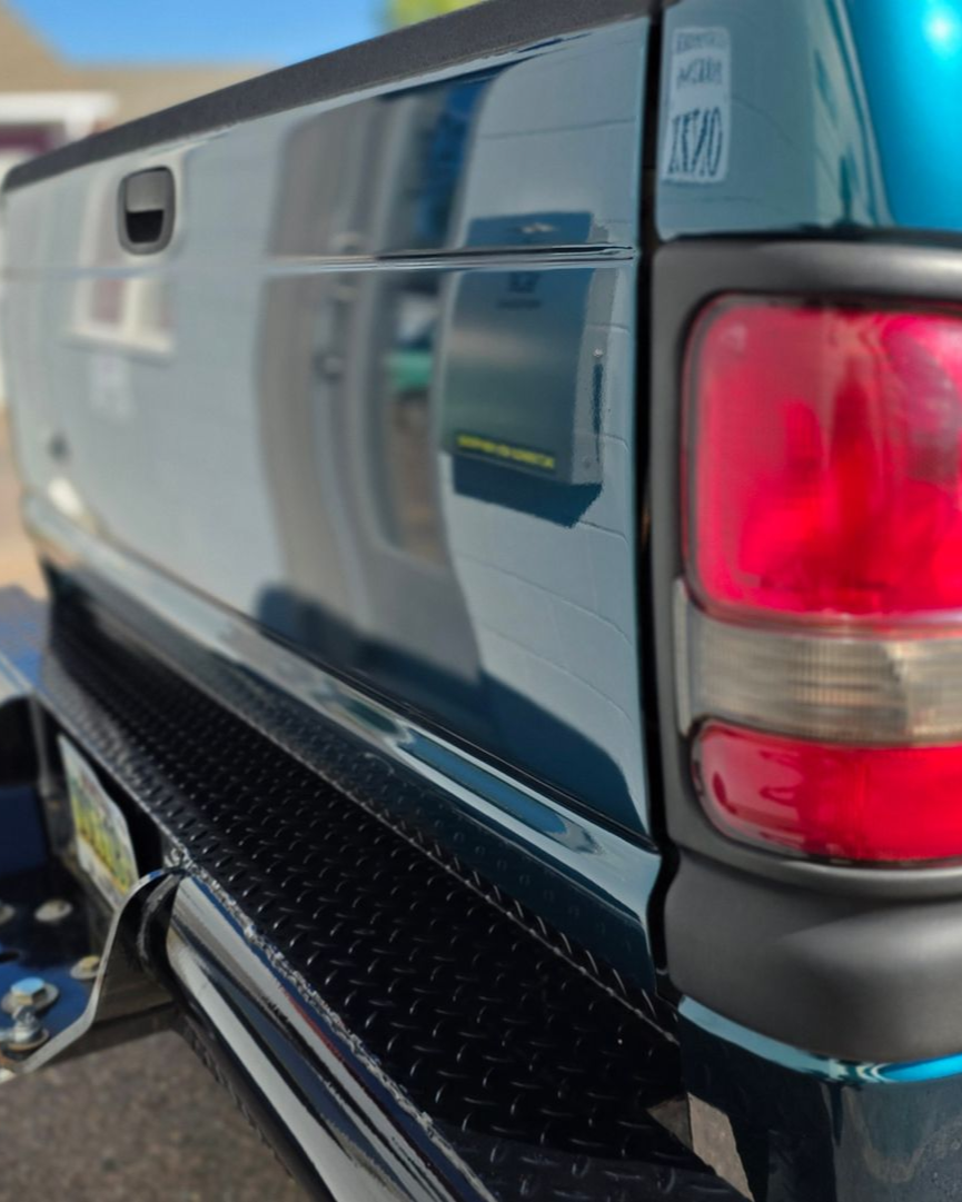 Close-up of a blue pickup truck’s rear corner with red taillight and black step bumper.