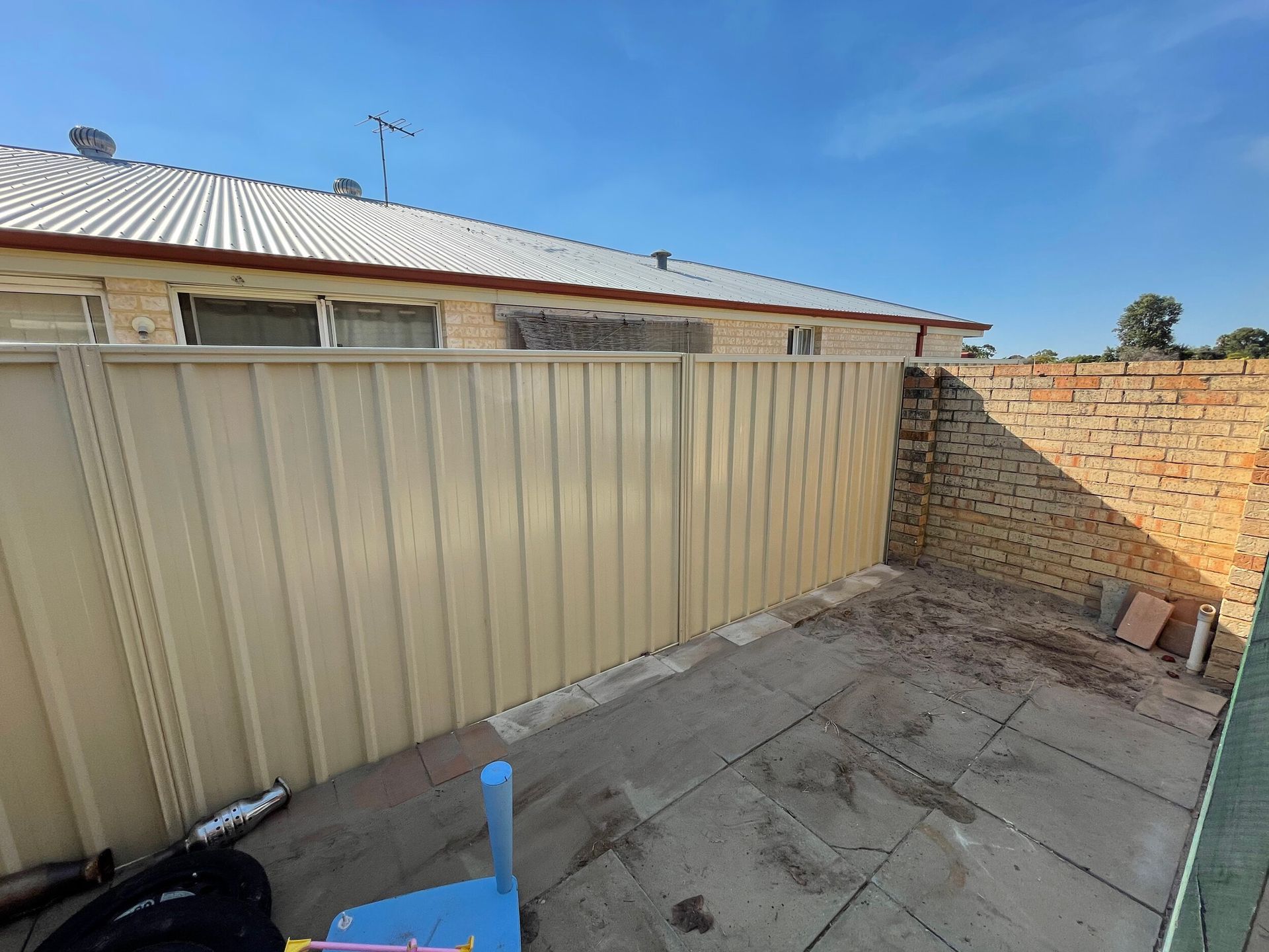 Small paved courtyard with beige fence, brick wall, and blue sky.