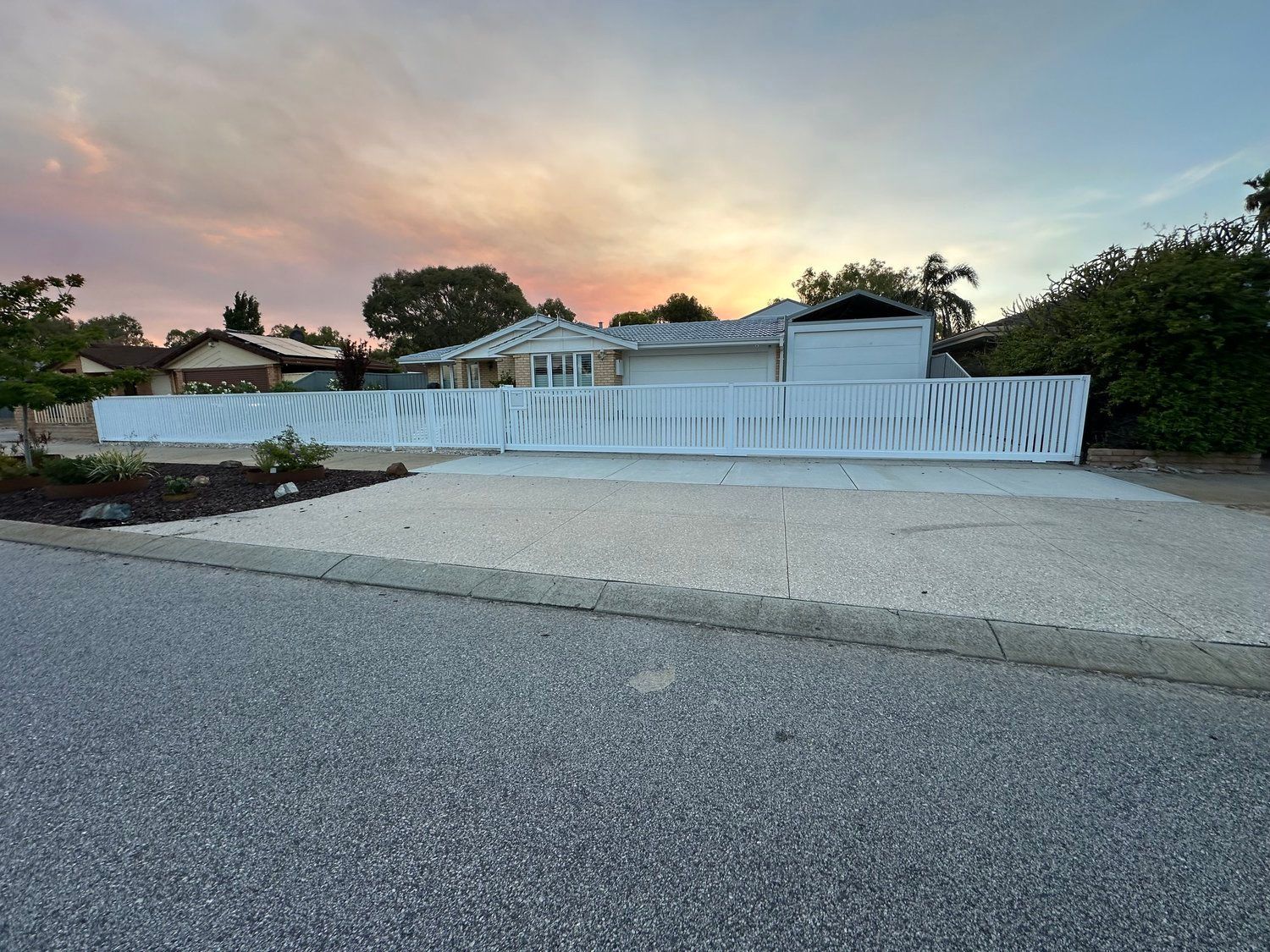 White fence and house at sunset beside a gravel driveway and road