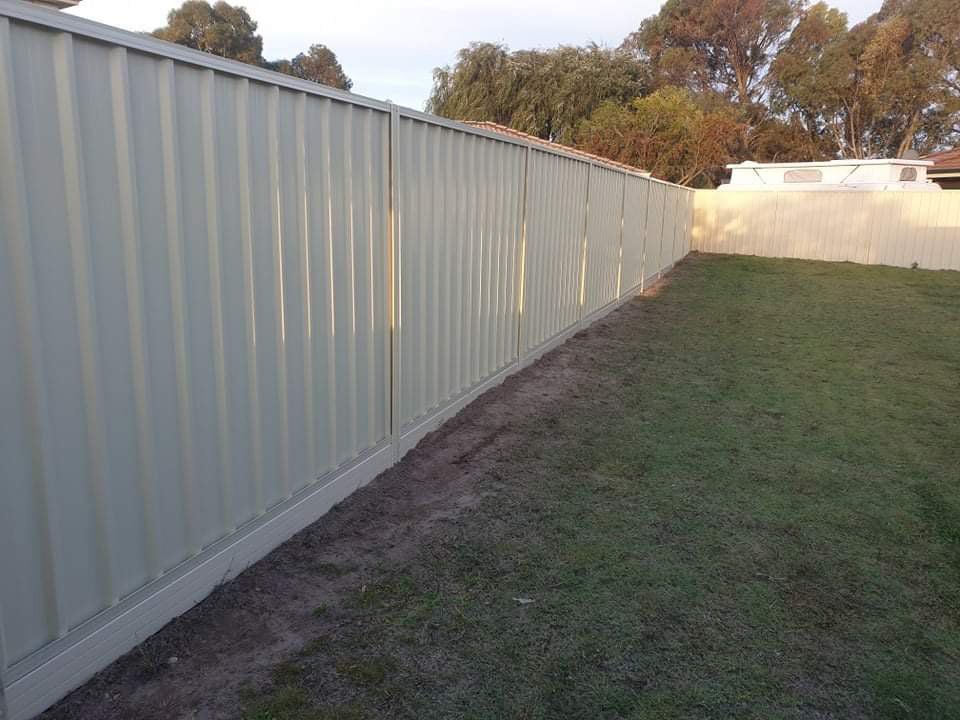 Long white fence lining a grassy yard beside trees and a building at sunset