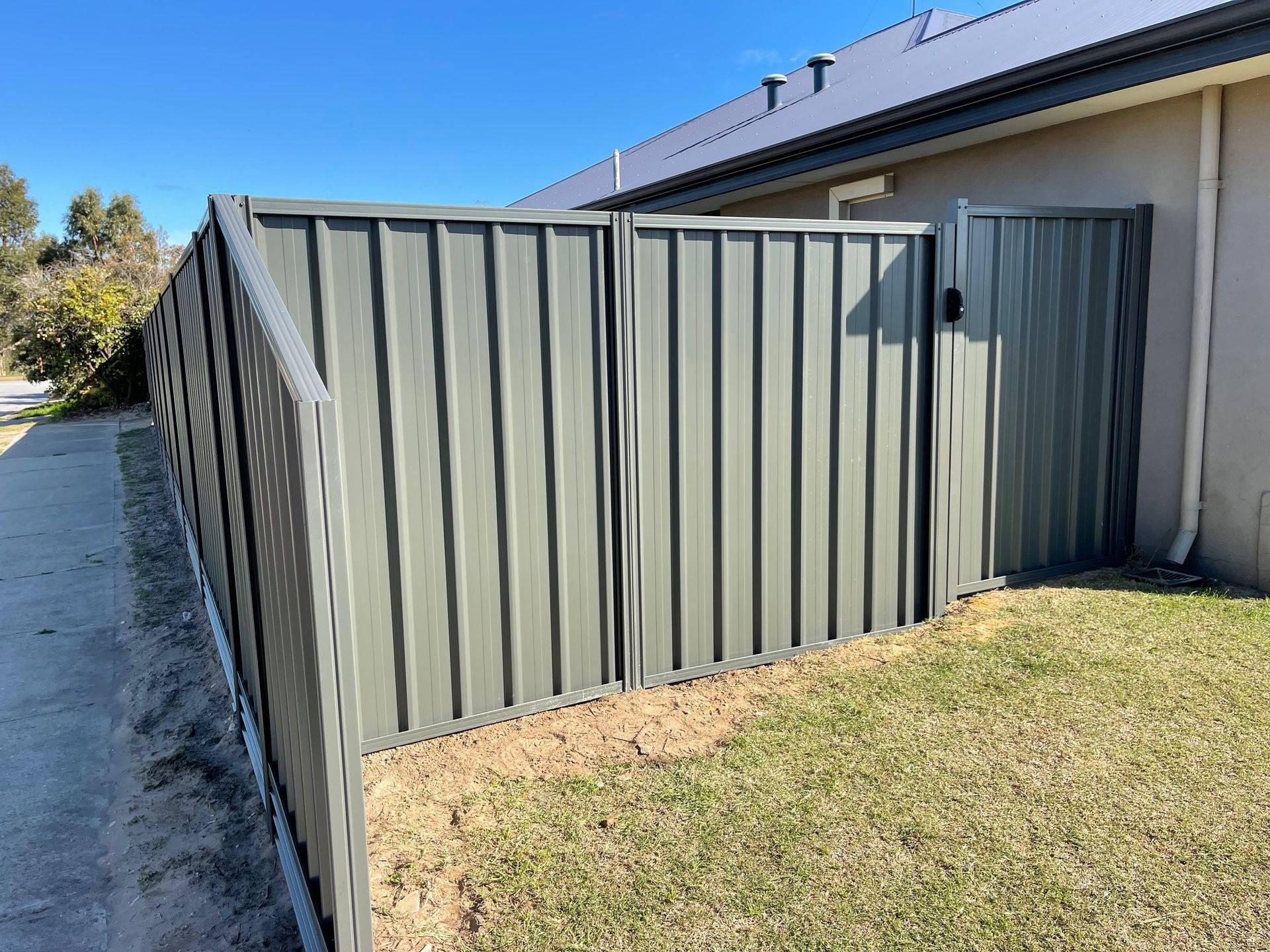 Gray metal fence enclosing a small side yard beside a house, with grass and a concrete driveway.