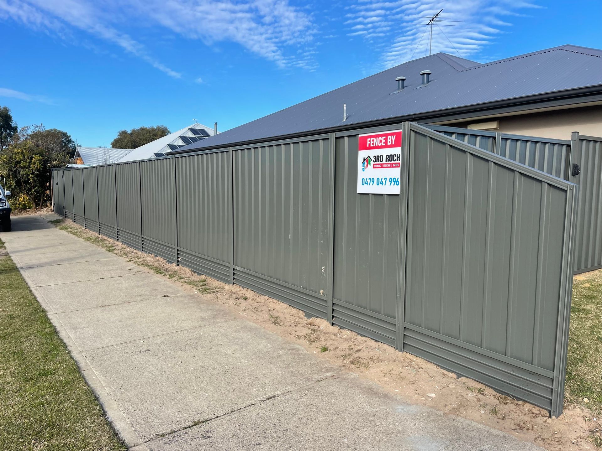 Gray metal fence along a sidewalk beside a house under a blue sky, with a property sign attached.
