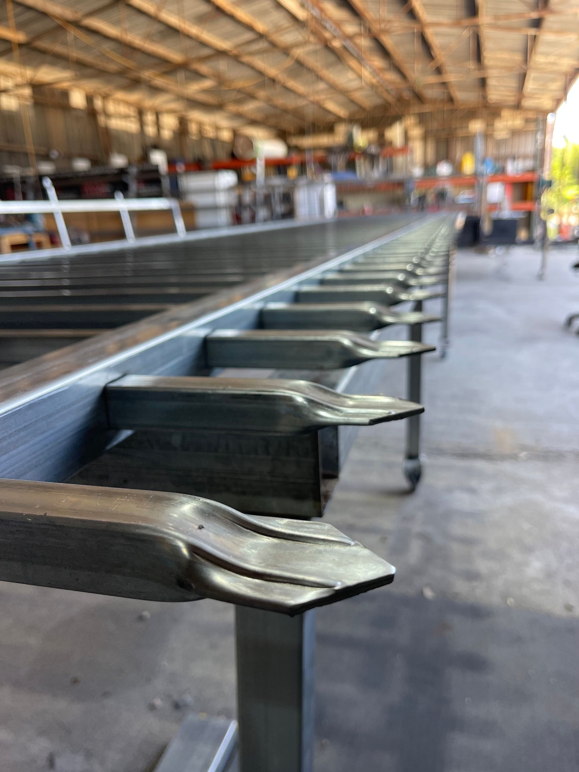 Metal conveyor-like rail in an industrial workshop, viewed in perspective with a blurred factory background