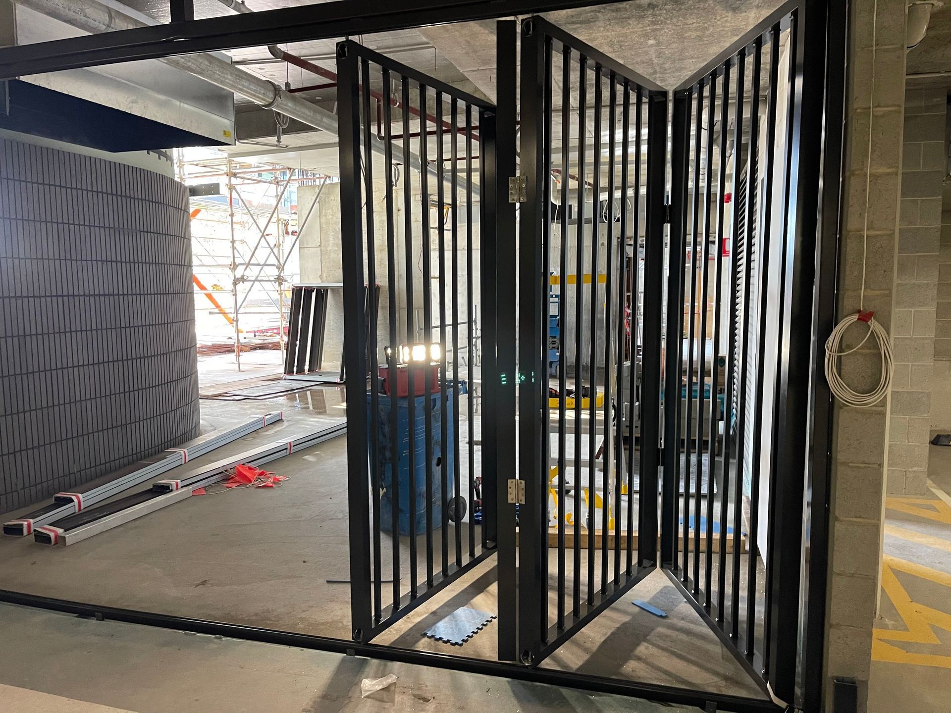 Black metal security gate in an industrial parking area, with a large vehicle tire and construction materials nearby