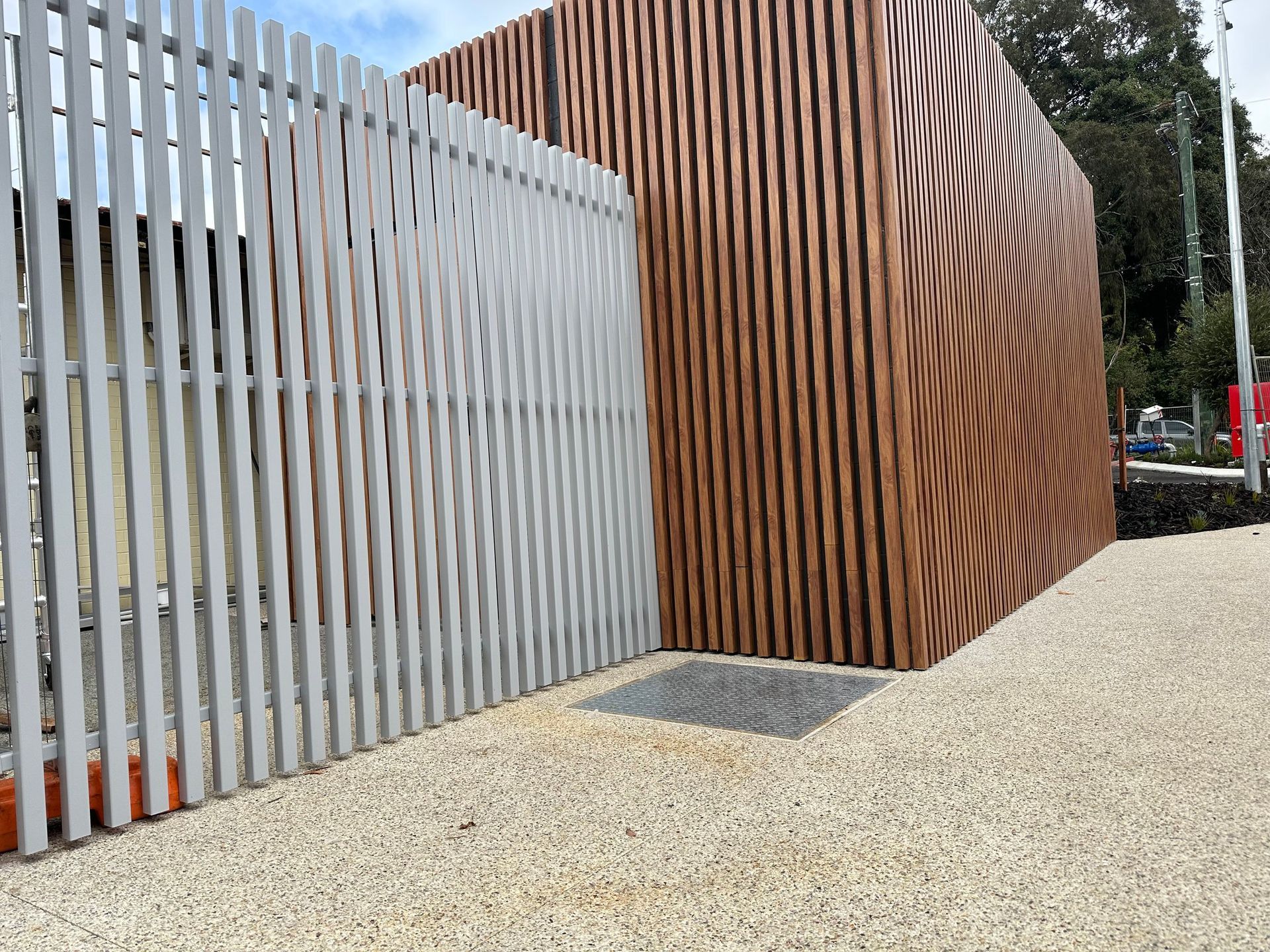 Modern outdoor entrance with vertical metal and wood slat panels beside a gravel path
