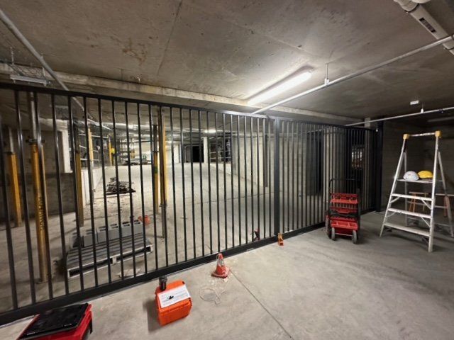 Construction area with black metal gate, ladder, orange cone, and a red tool cart in a concrete garage.
