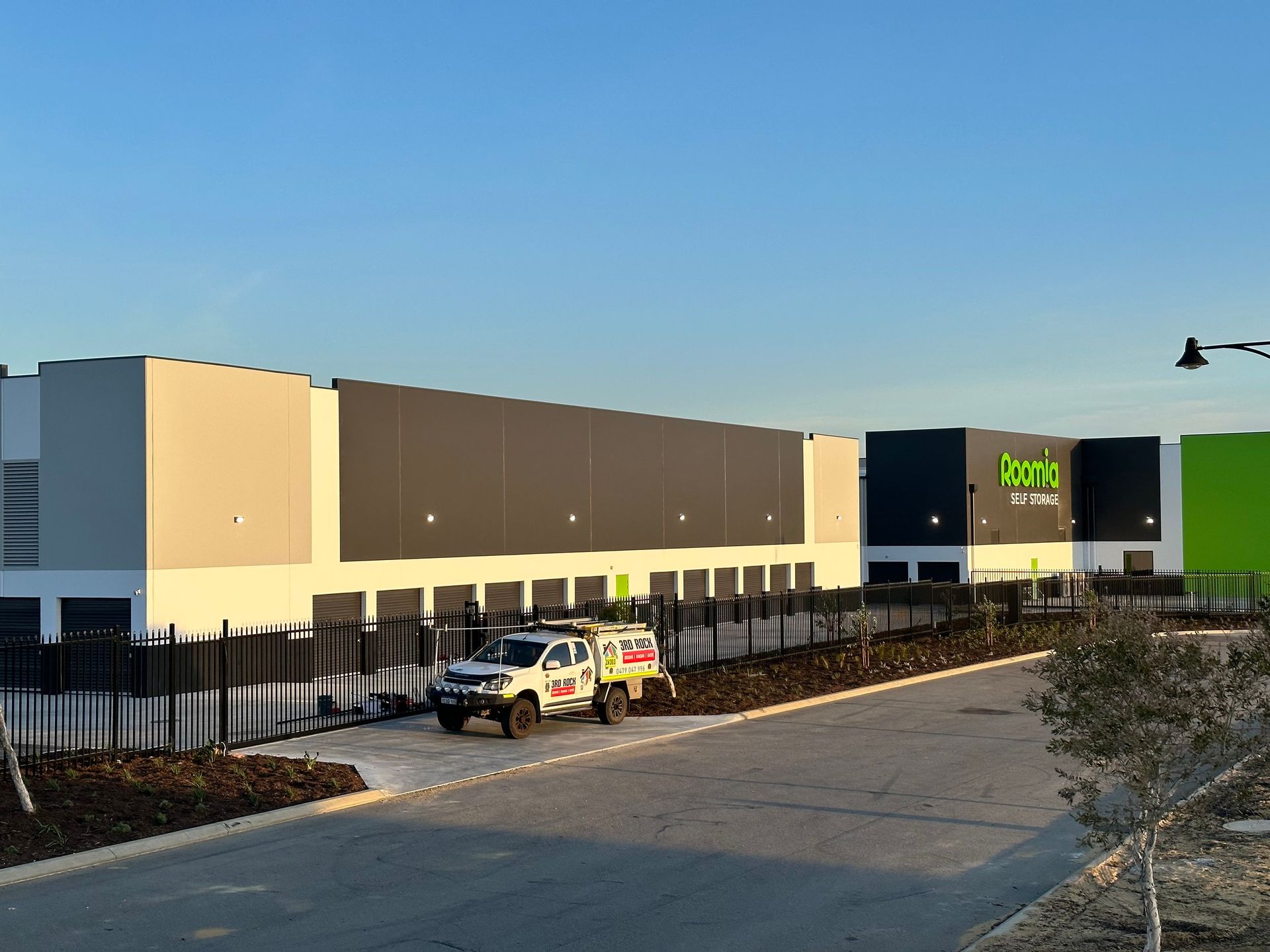 Storefront exterior with black-and-beige facade, fenced parking lot, and a service truck at dusk