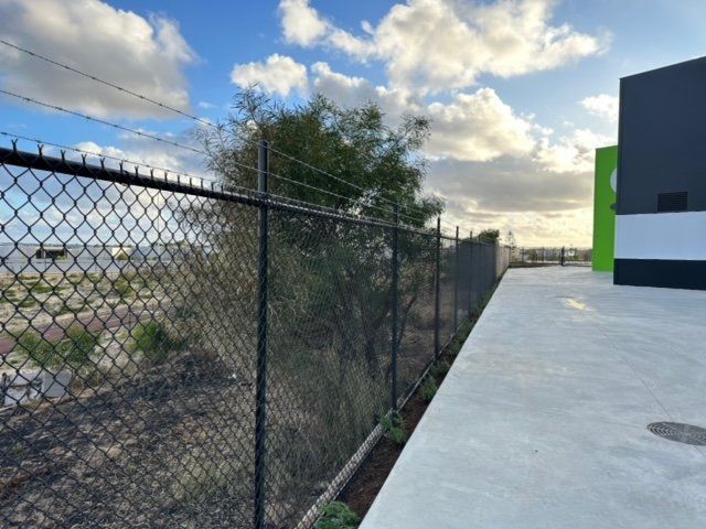 Chain-link fence beside a concrete walkway next to a building under a cloudy sky