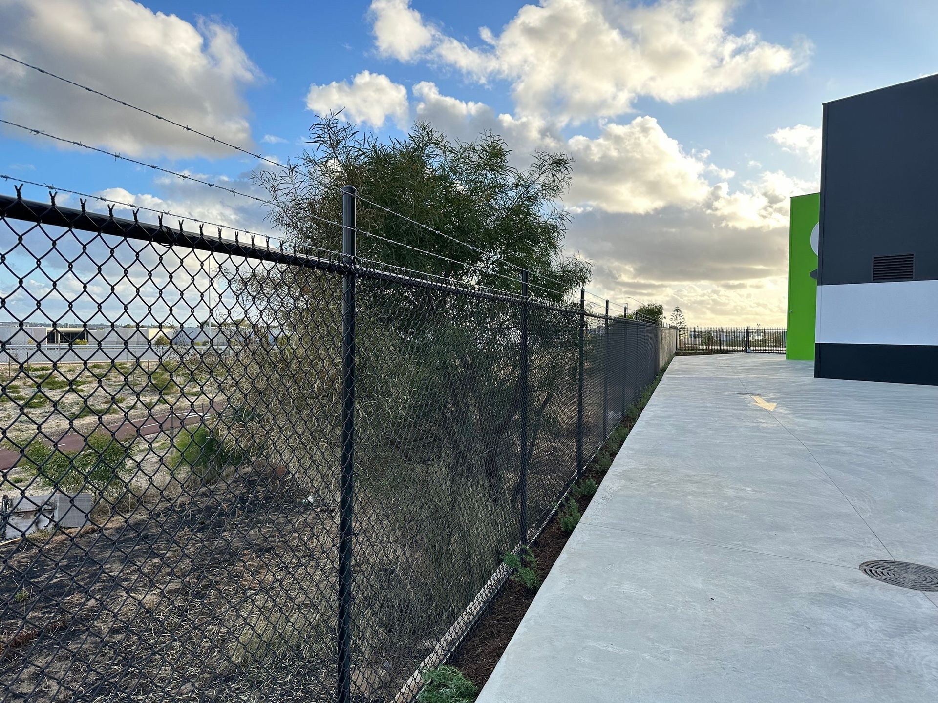 Chain-link fence beside a concrete walkway next to a modern building under a cloudy sky