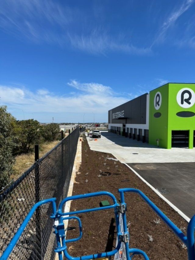 Bicycle handlebar view of a paved path beside a green building under a bright blue sky