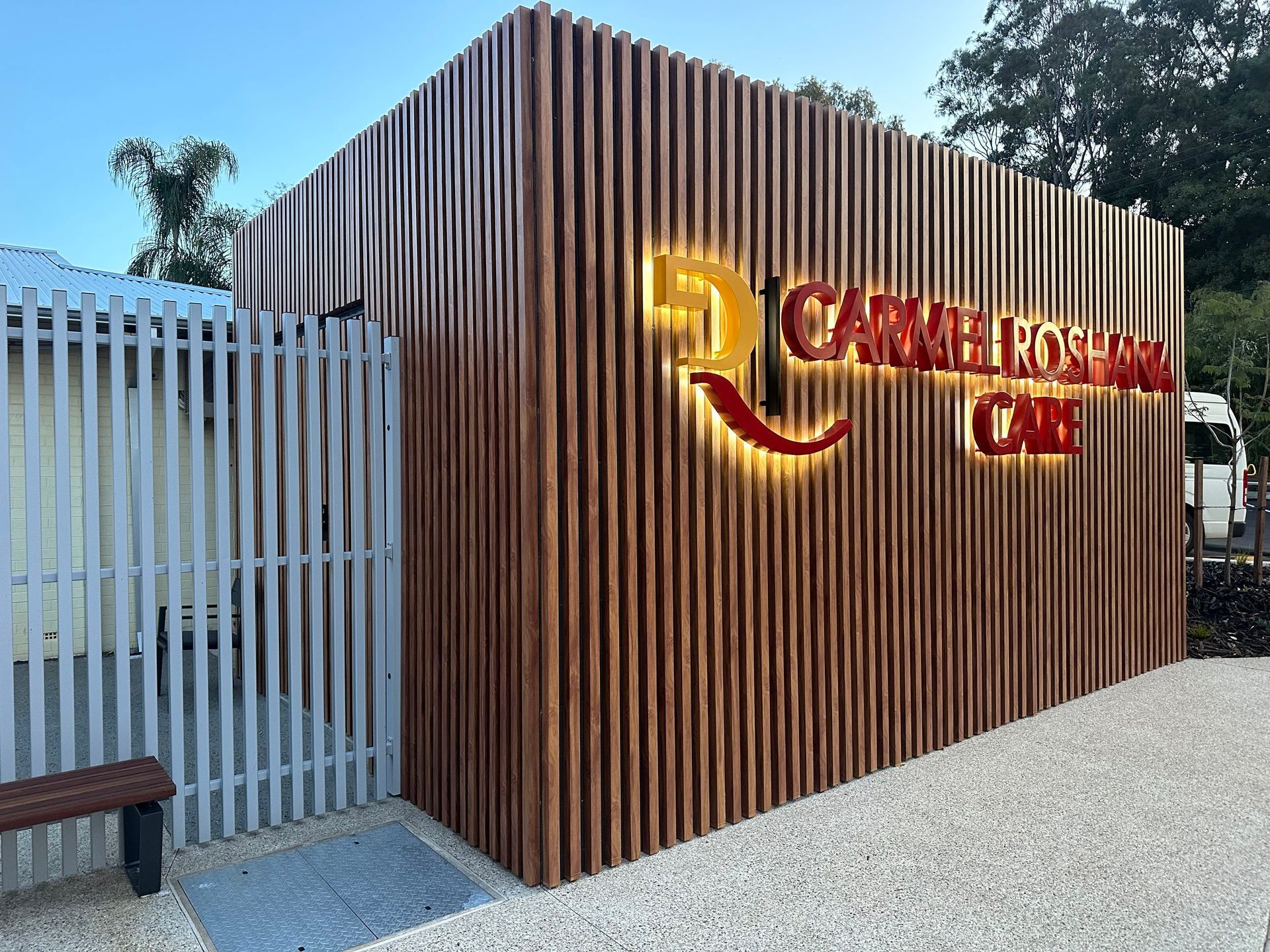 Wood-paneled entrance wall with lit red-and-gold “CANDER ROCKS CAFE” sign beside a white gate