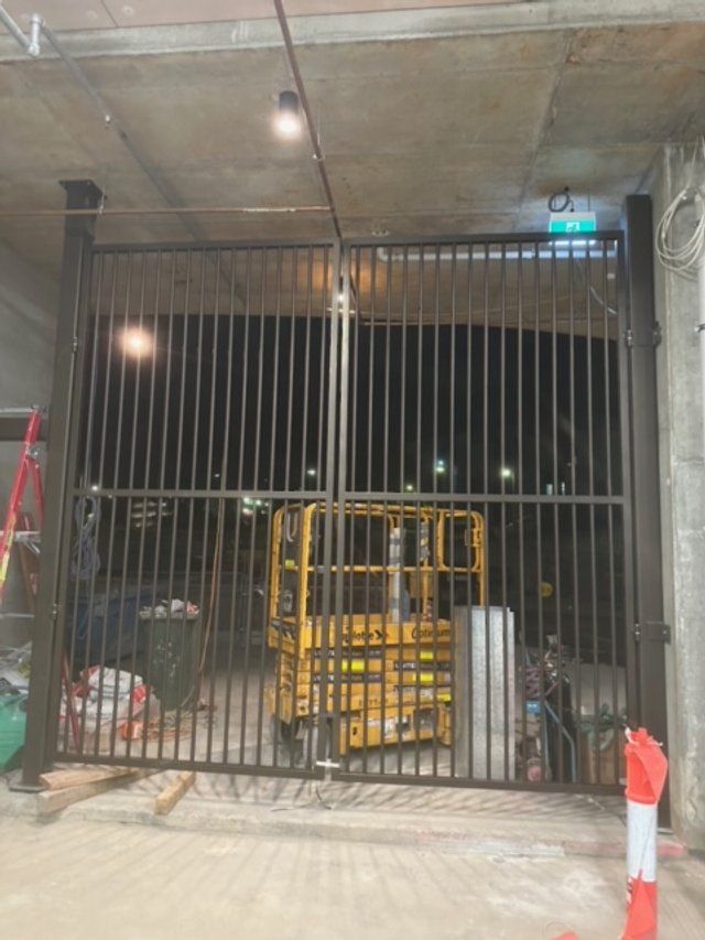 Industrial storage area behind tall black metal security gate with stacked yellow pallets inside