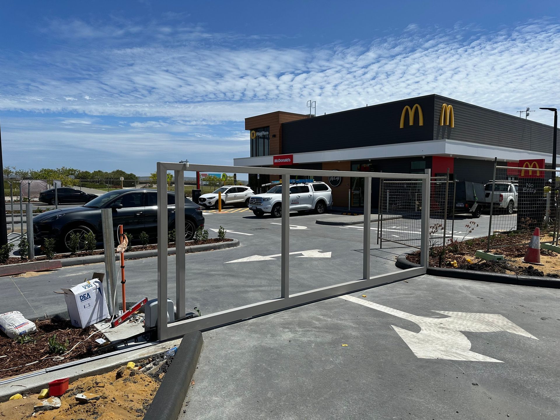 McDonald’s drive-thru entrance with a fenced-off construction area and parked cars under a blue sky