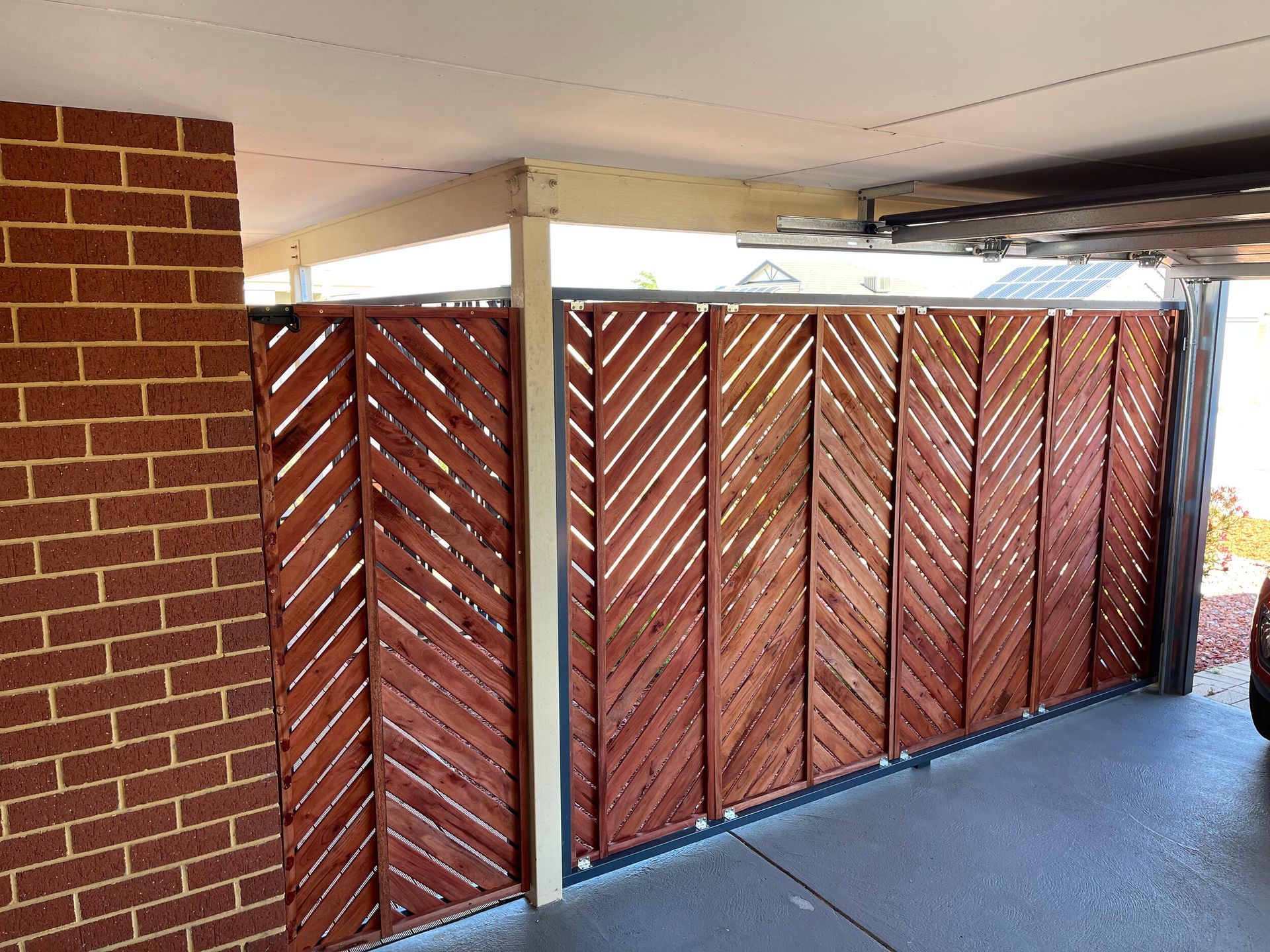 Covered patio with red brick wall and brown wooden slatted privacy screens above a concrete floor