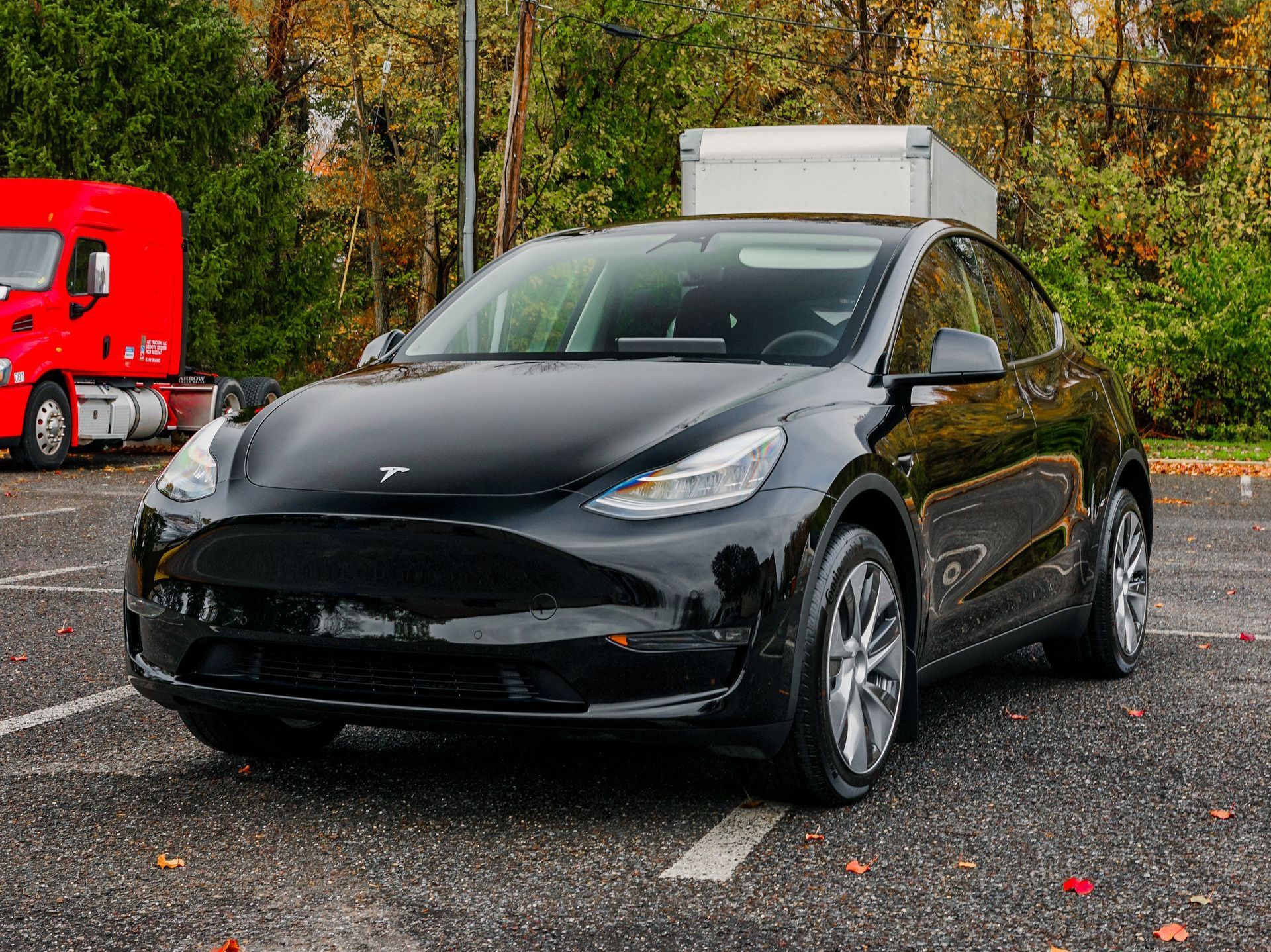 A black tesla model y is parked in a parking lot next to a red truck.