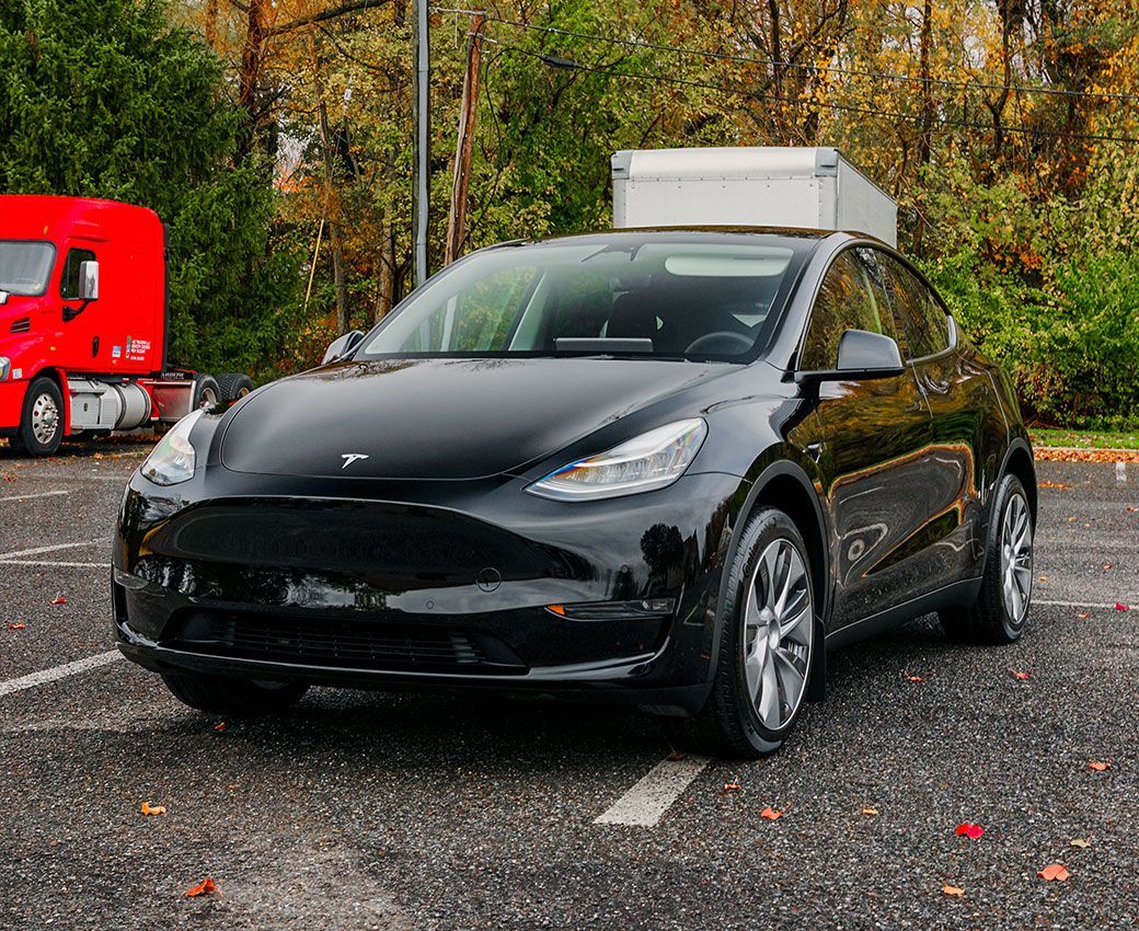 A black tesla model y is parked in a parking lot next to a red truck.
