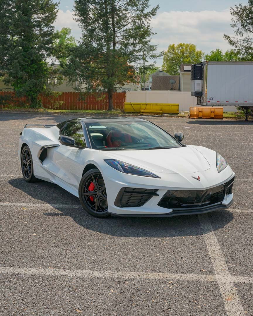 White convertible sports car parked in a lot, red brake calipers, black wheels, sunny day.