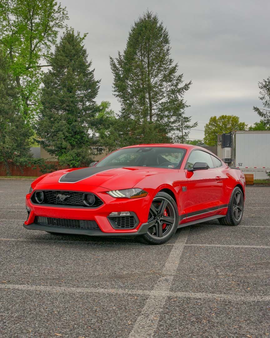 Red Ford Mustang sports car parked on asphalt, black stripe on hood.