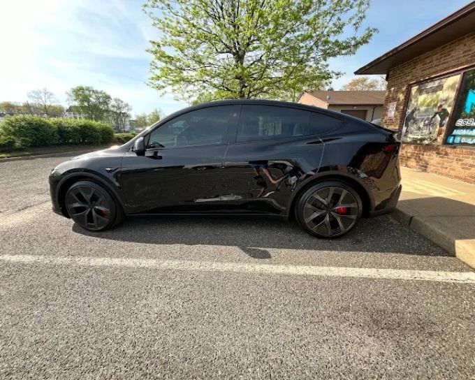 Black luxury sedan with sleek window tint and glossy finish parked outside a detailing shop.