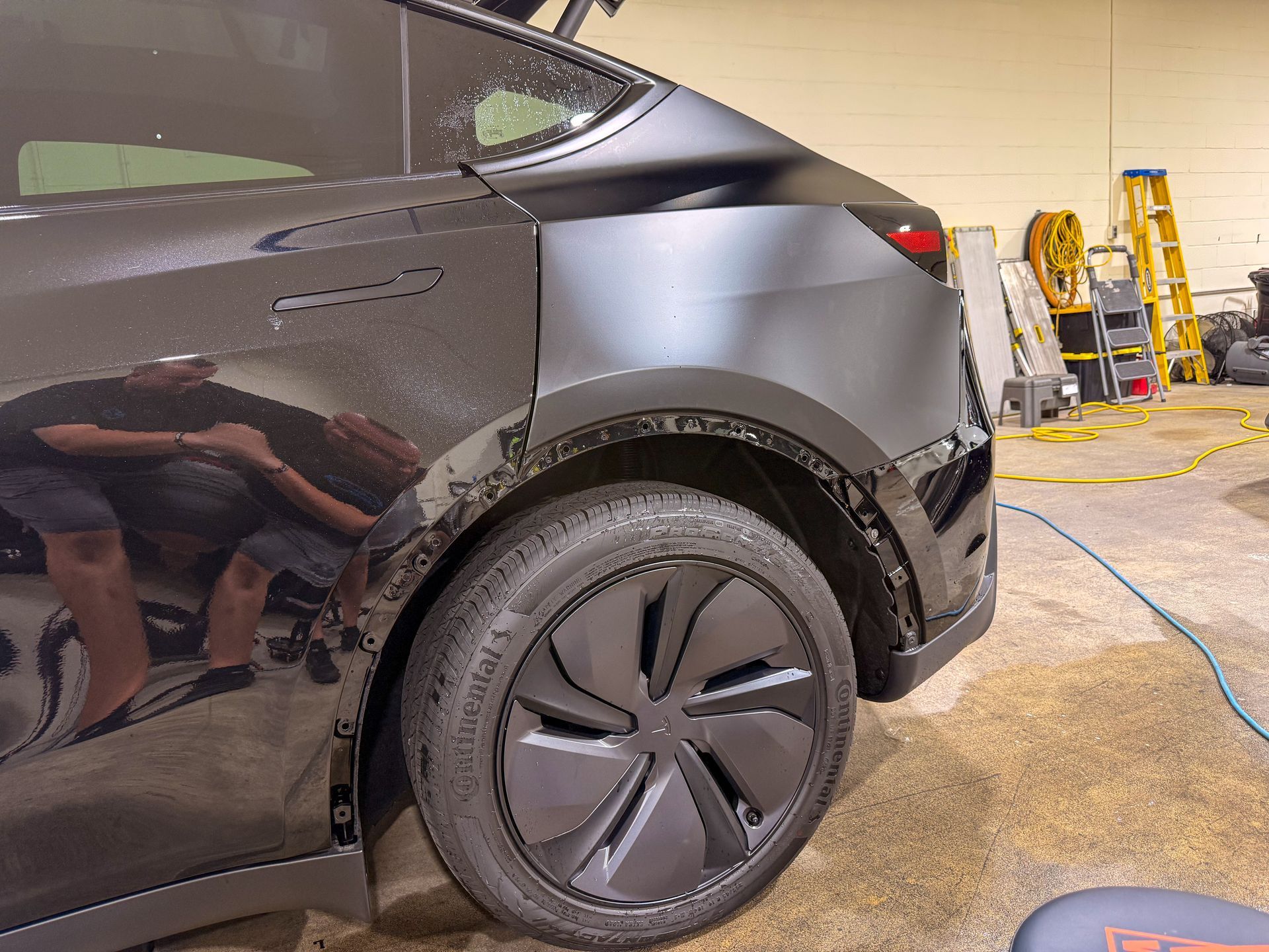 Black car rear wheel in auto shop with tools and equipment nearby