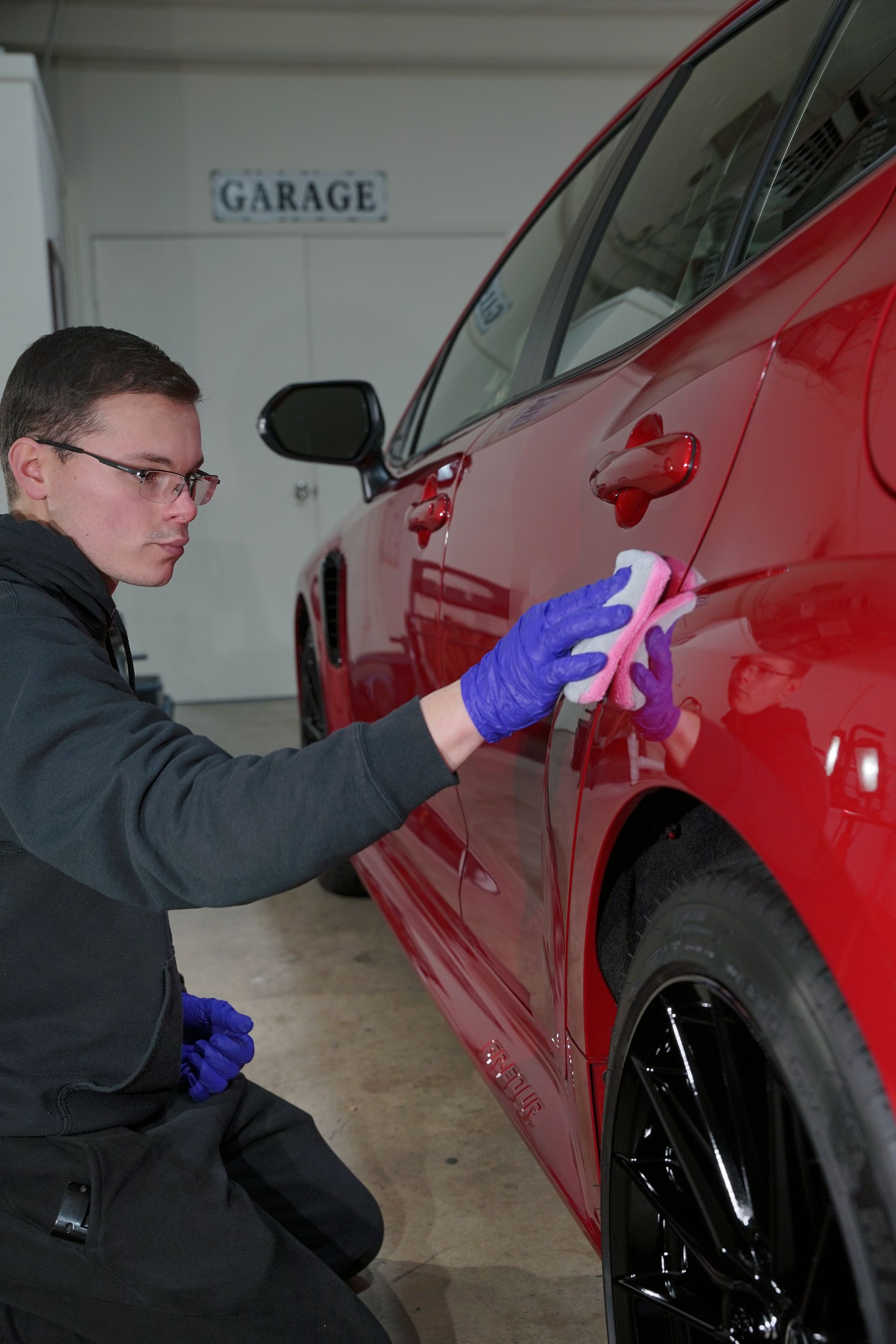 a man cleaning a red car in front of a garage sign