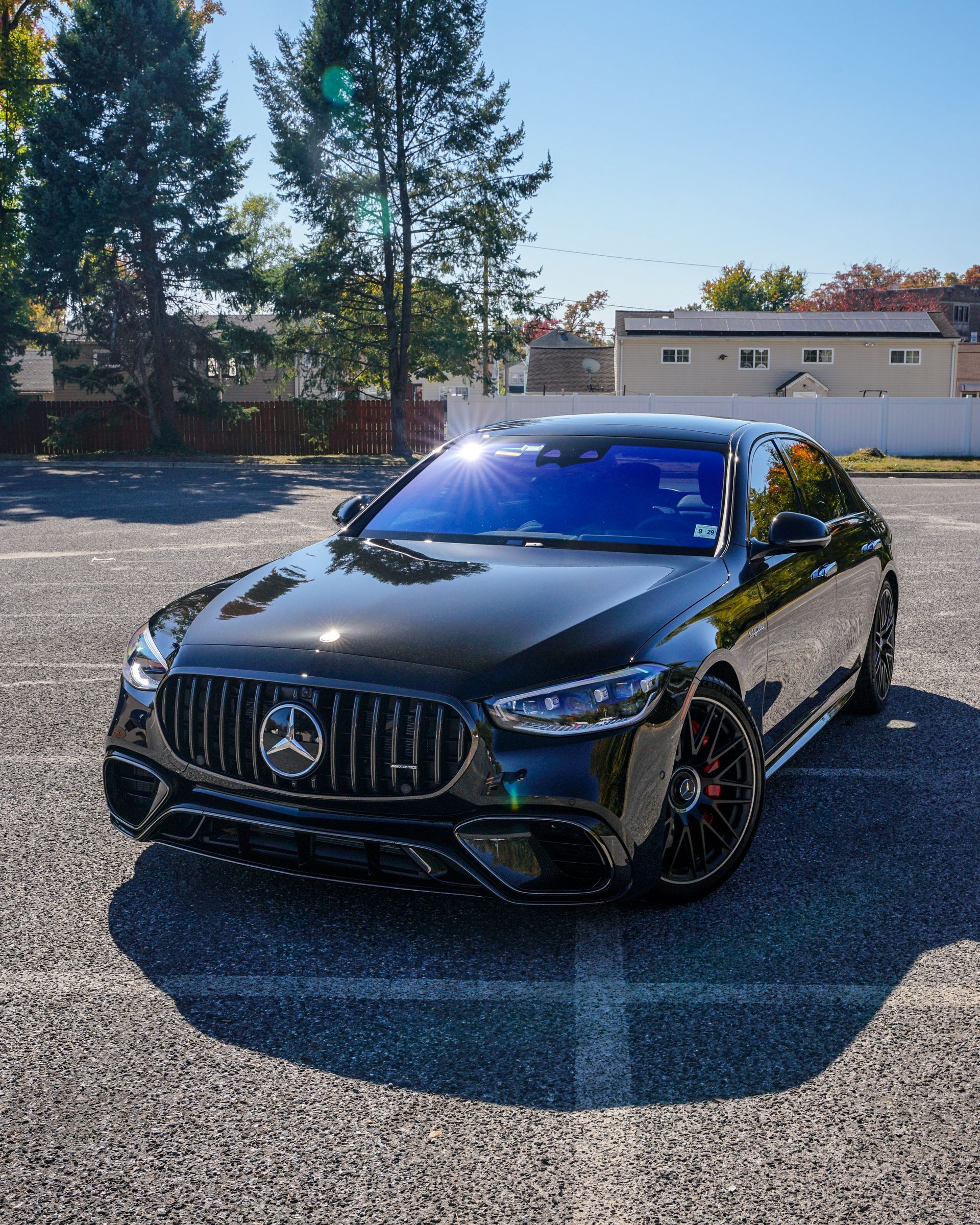 A sleek, black Mercedes-Benz sedan parked on a gravel lot under a bright, sunny sky.