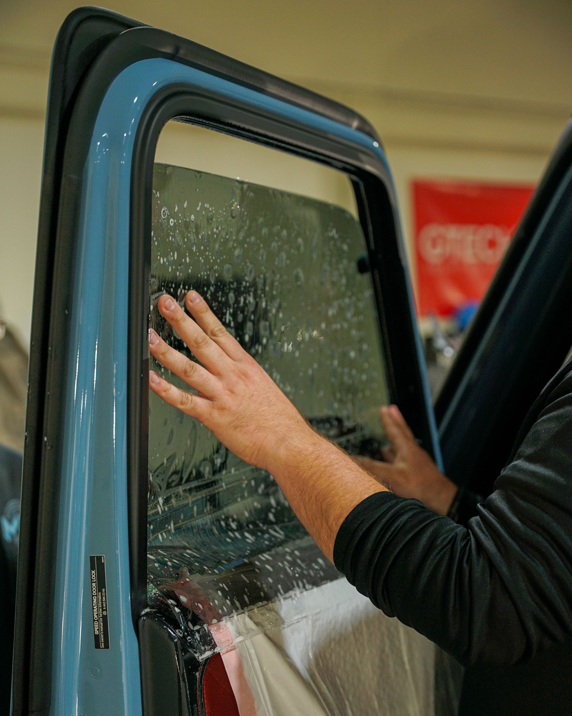 Person applying window tint to a car window, hands smoothing film on glass.