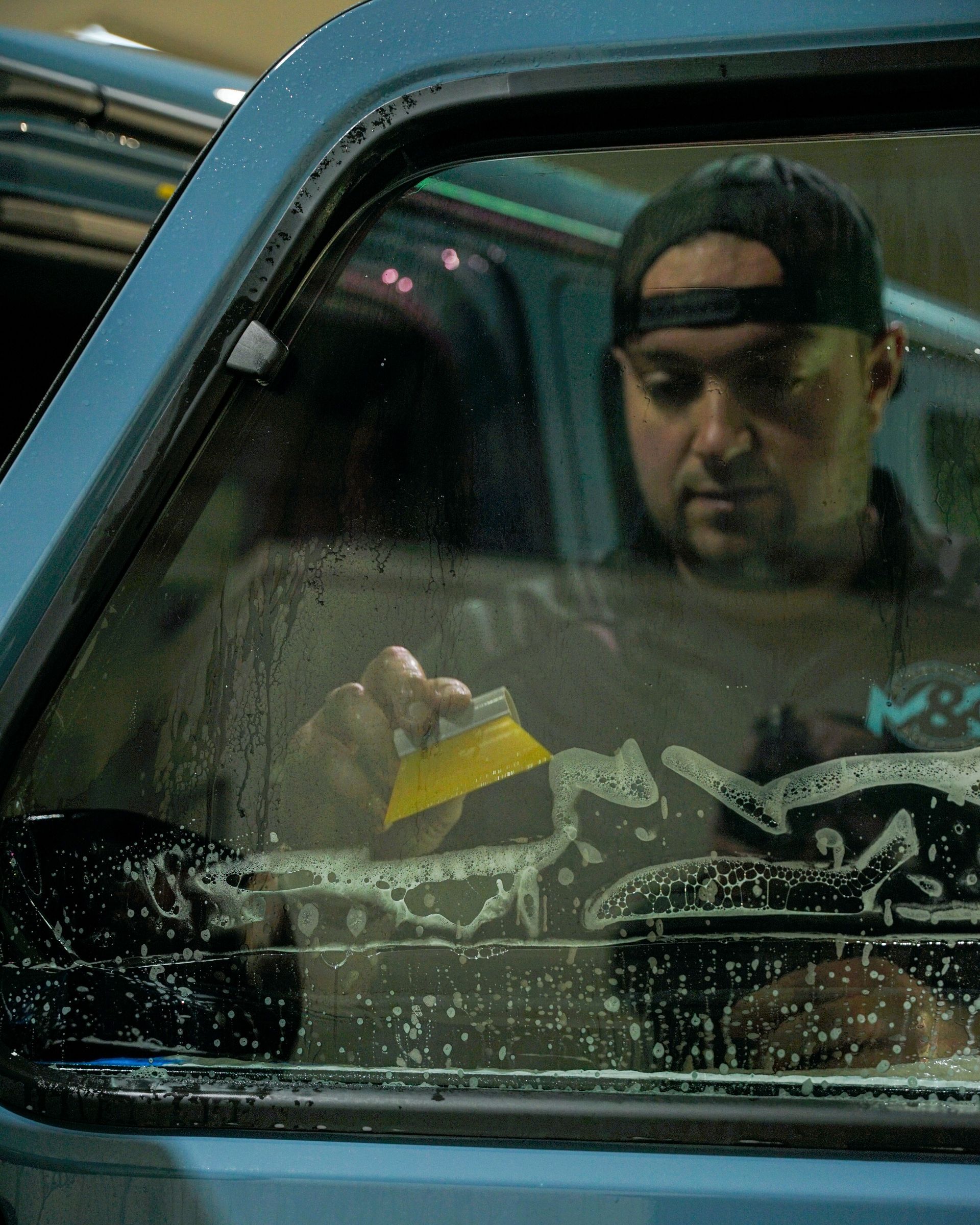Man applying window tint to a car window with a yellow squeegee.
