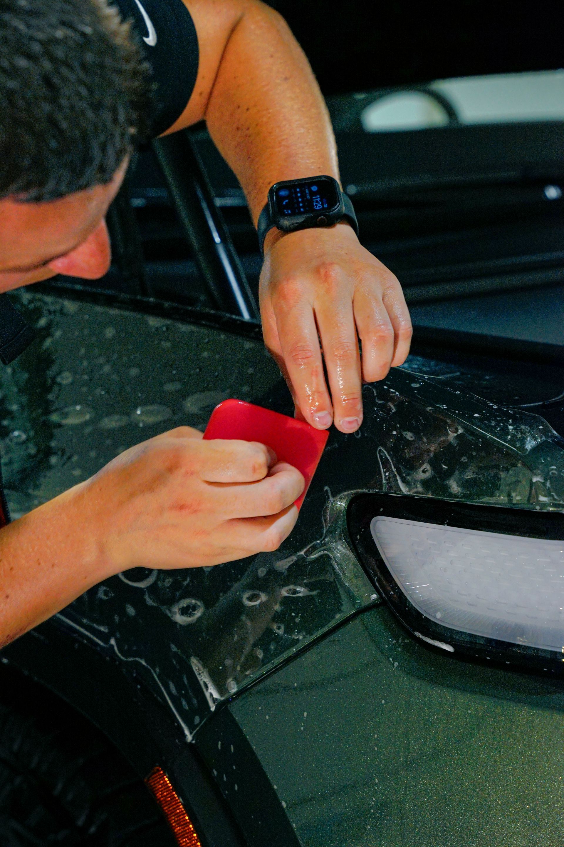 Person using a red squeegee to apply clear film to a car's surface.