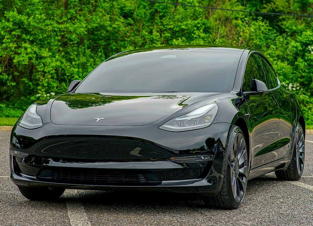 A black tesla model 3 is parked on the side of the road.