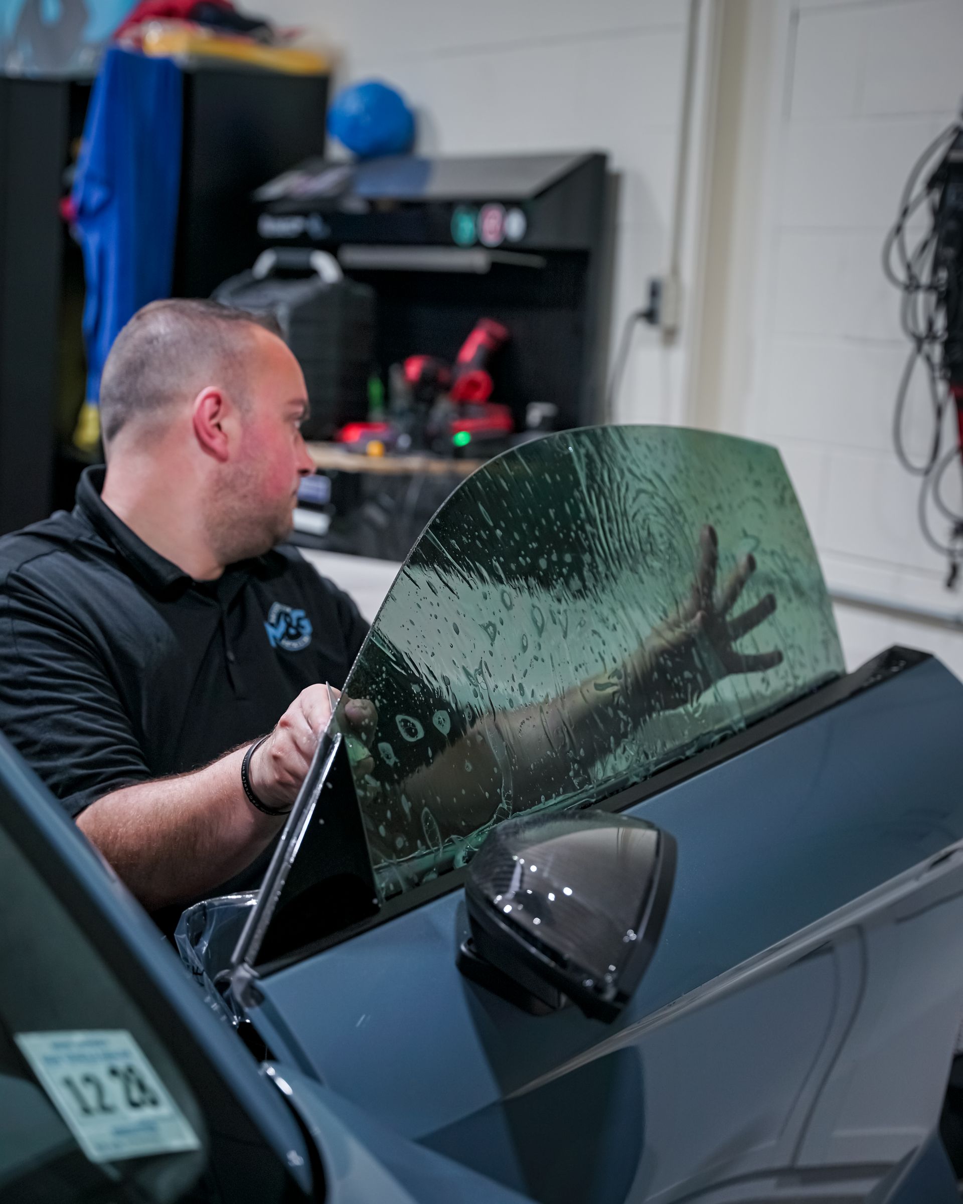 A man installing window tint on a car window. He is holding the tinted film with his hands.