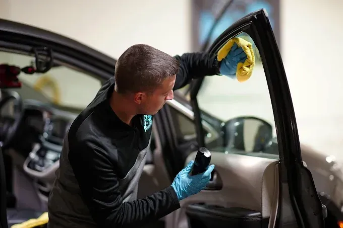 Technician wearing gloves applying auto window tint film to a car's rear door window