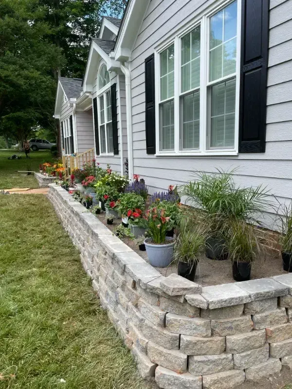 A house with a brick wall and potted plants in front of it.