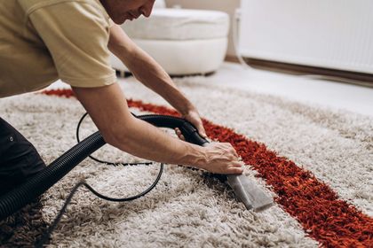 Person cleans a carpet with a handheld cleaning tool; the carpet has white and red stripes. Person cleans a carpet with a handheld cleaning tool; the carpet has white and red stripes.