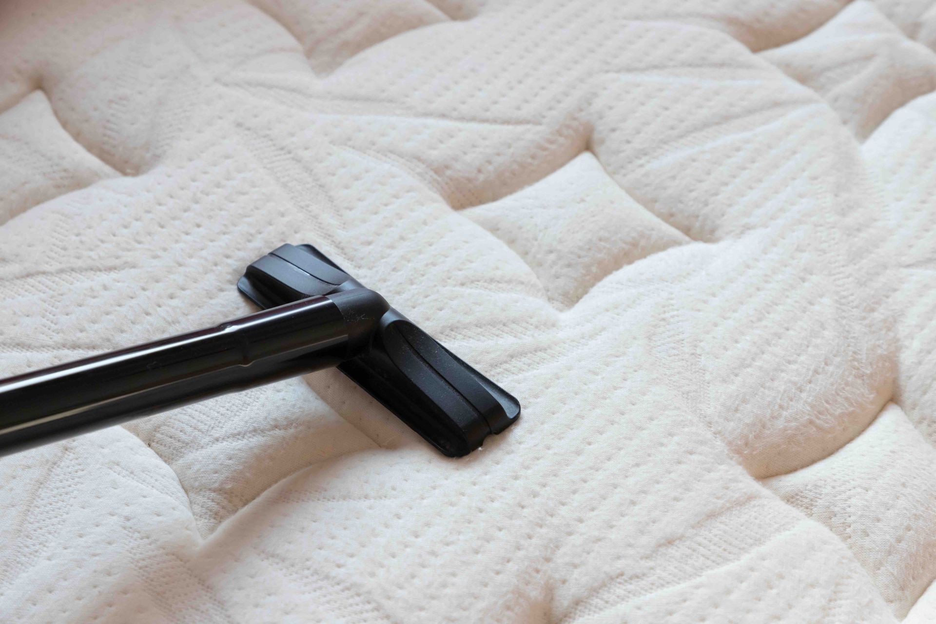 Vacuum cleaner cleaning a white, tufted mattress.