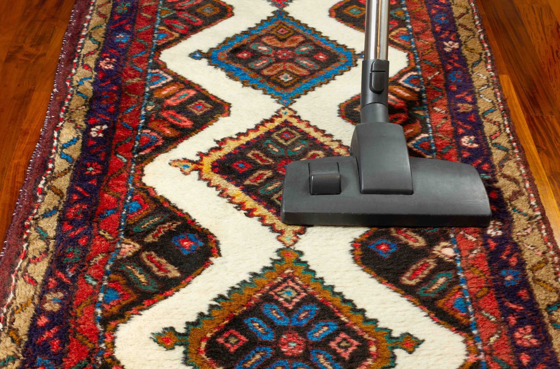 Vacuum cleaner cleaning a patterned, colorful rug on a wooden floor.