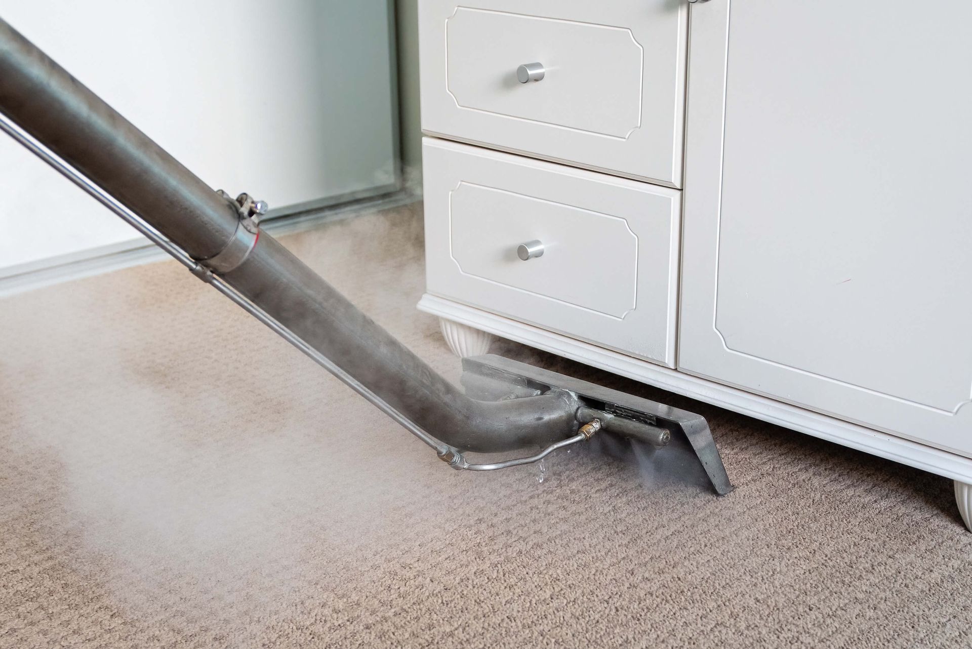Steam cleaner on beige carpet by white cabinet.