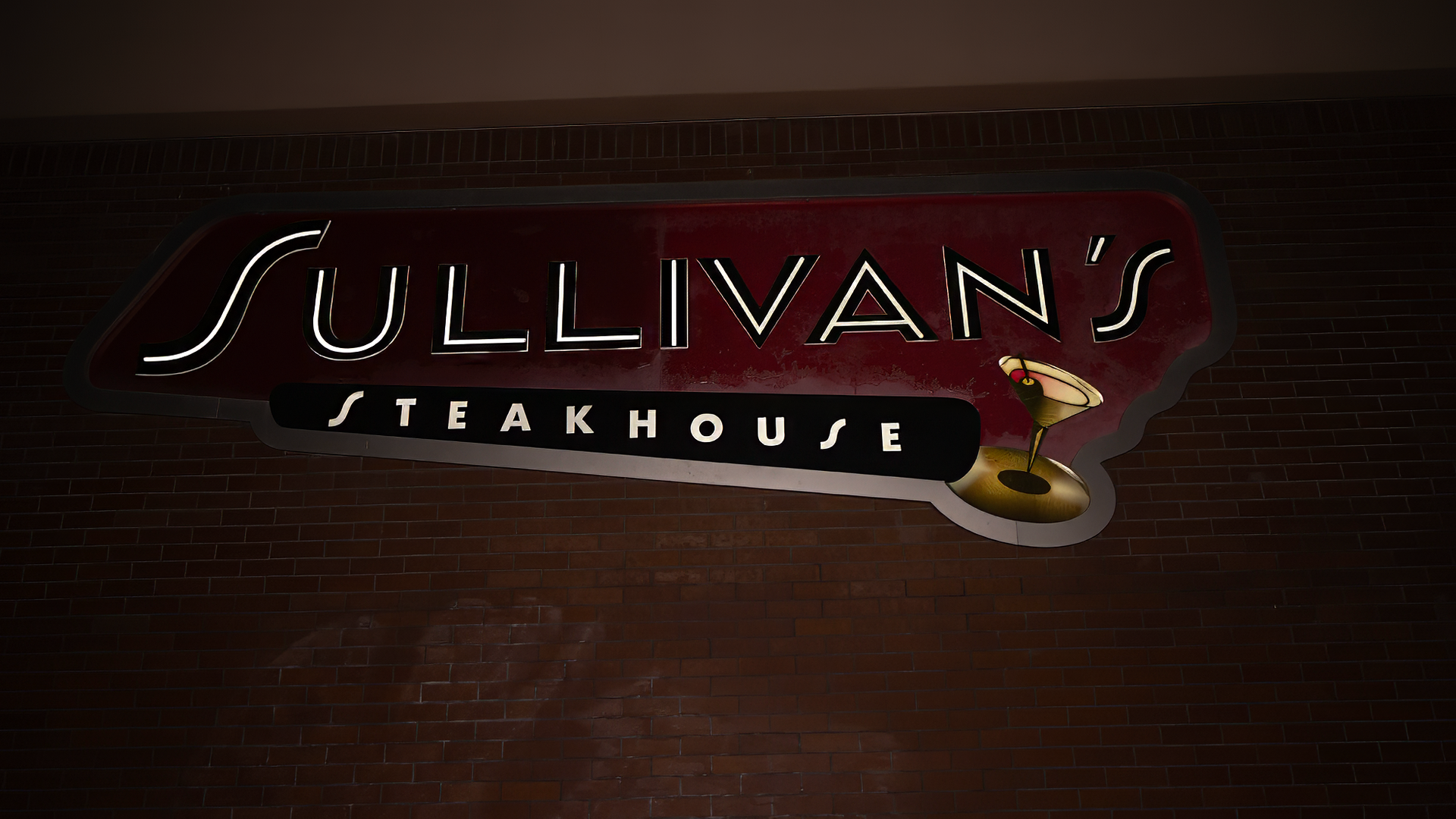 Sullivan's Steakhouse sign, red and white neon, on a dark brown wall.