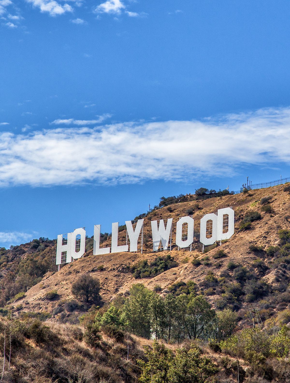 Hollywood sign on a brown hillside under a blue sky with scattered clouds.
