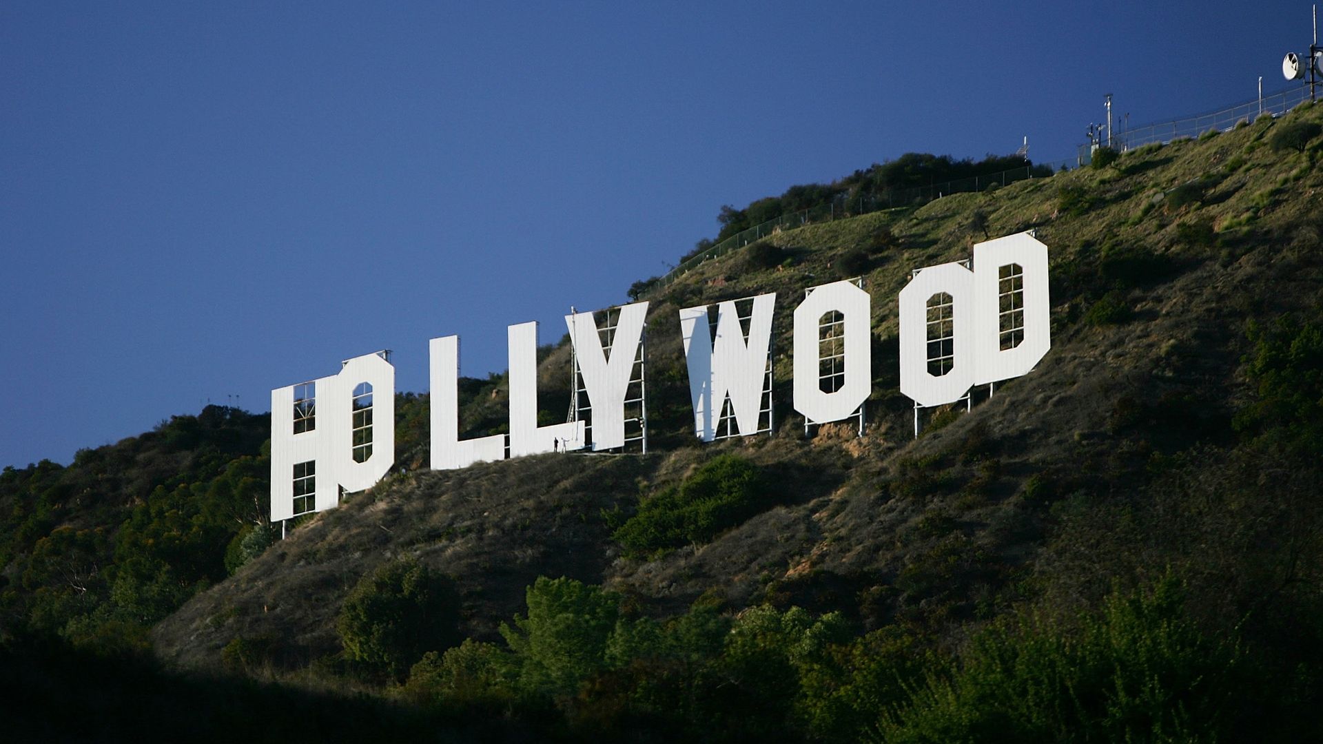 Hollywood sign on a hillside against a blue sky. White letters stand out from the green landscape.