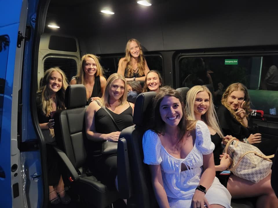 Group of women smiling inside a van, possibly on their way to a social event.